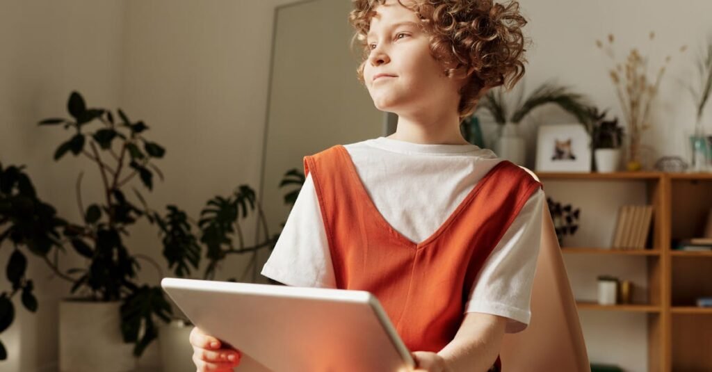 A young boy sits indoors holding a tablet, deep in thought, within a cozy home setting.