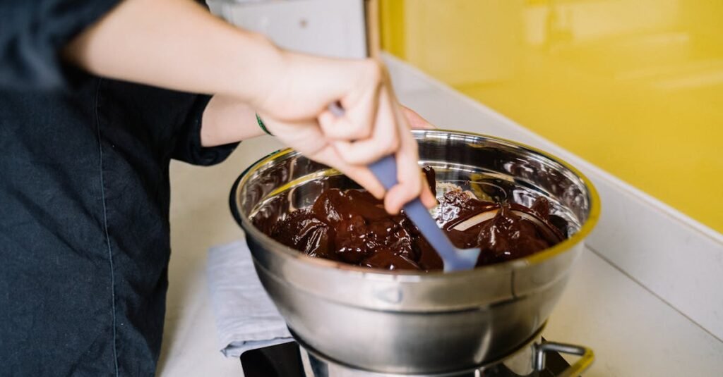 A person mixes rich melted chocolate in a stainless steel bowl for dessert preparation.