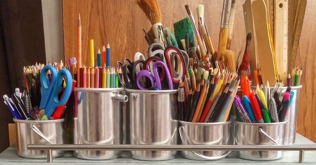 A diverse collection of art supplies in metallic buckets on a wooden table.