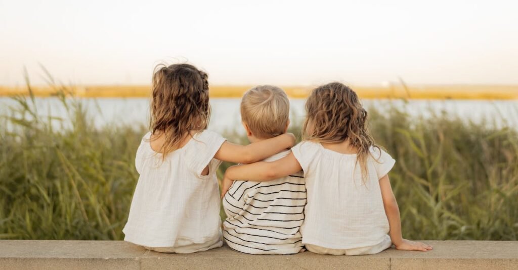Three children sit on a stone ledge, gazing at a serene lakeside scene, embodying friendship and tranquility.
